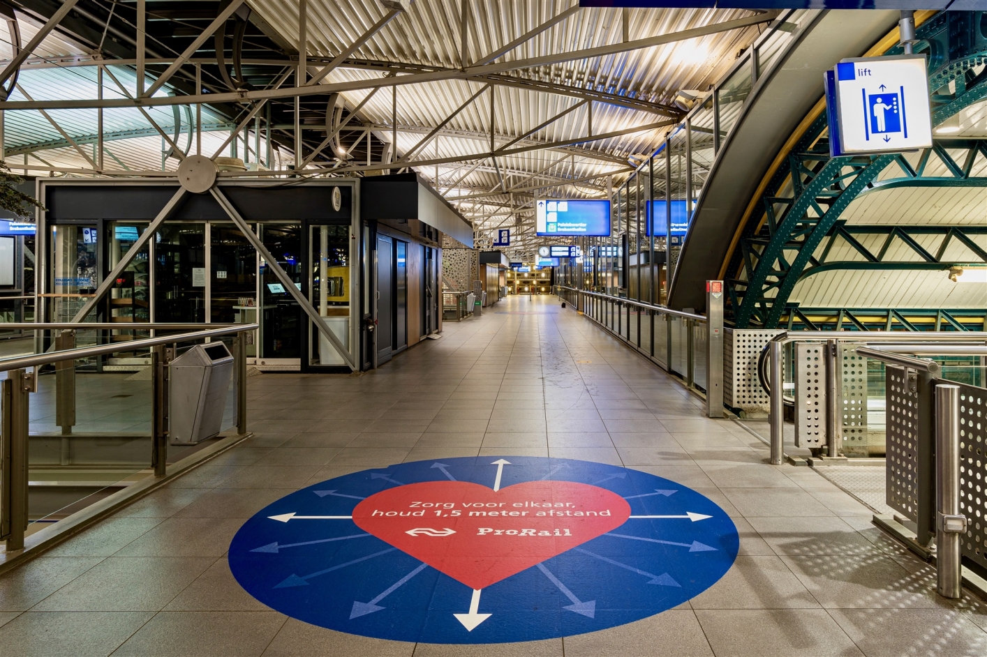 foto van stationstraverse met grote sticker op de grond met tekst 'Zorg voor elkaar, houd 1,5 m afstand'